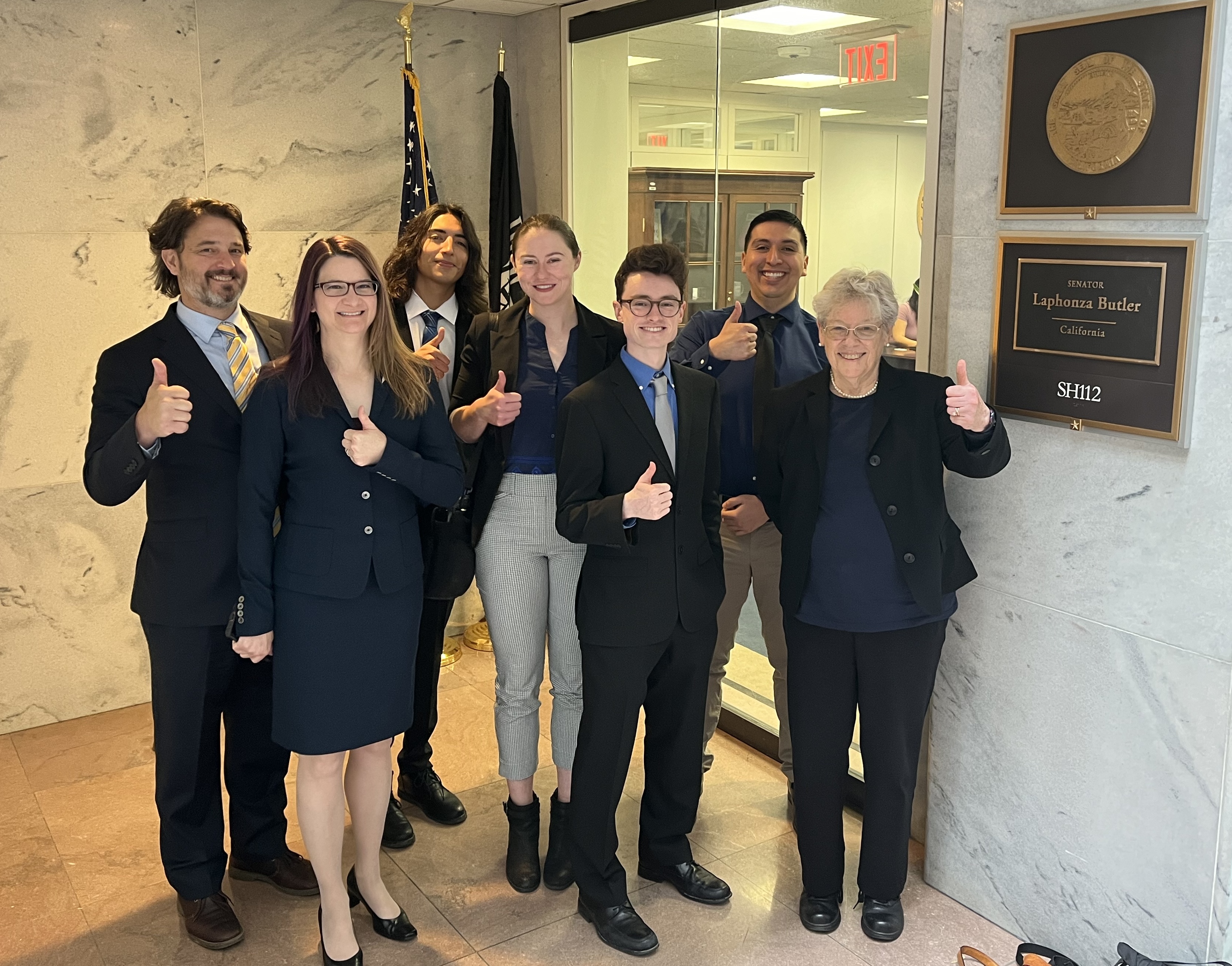 A group of graduate students and professors stand in front of a California sentator's office in DC.